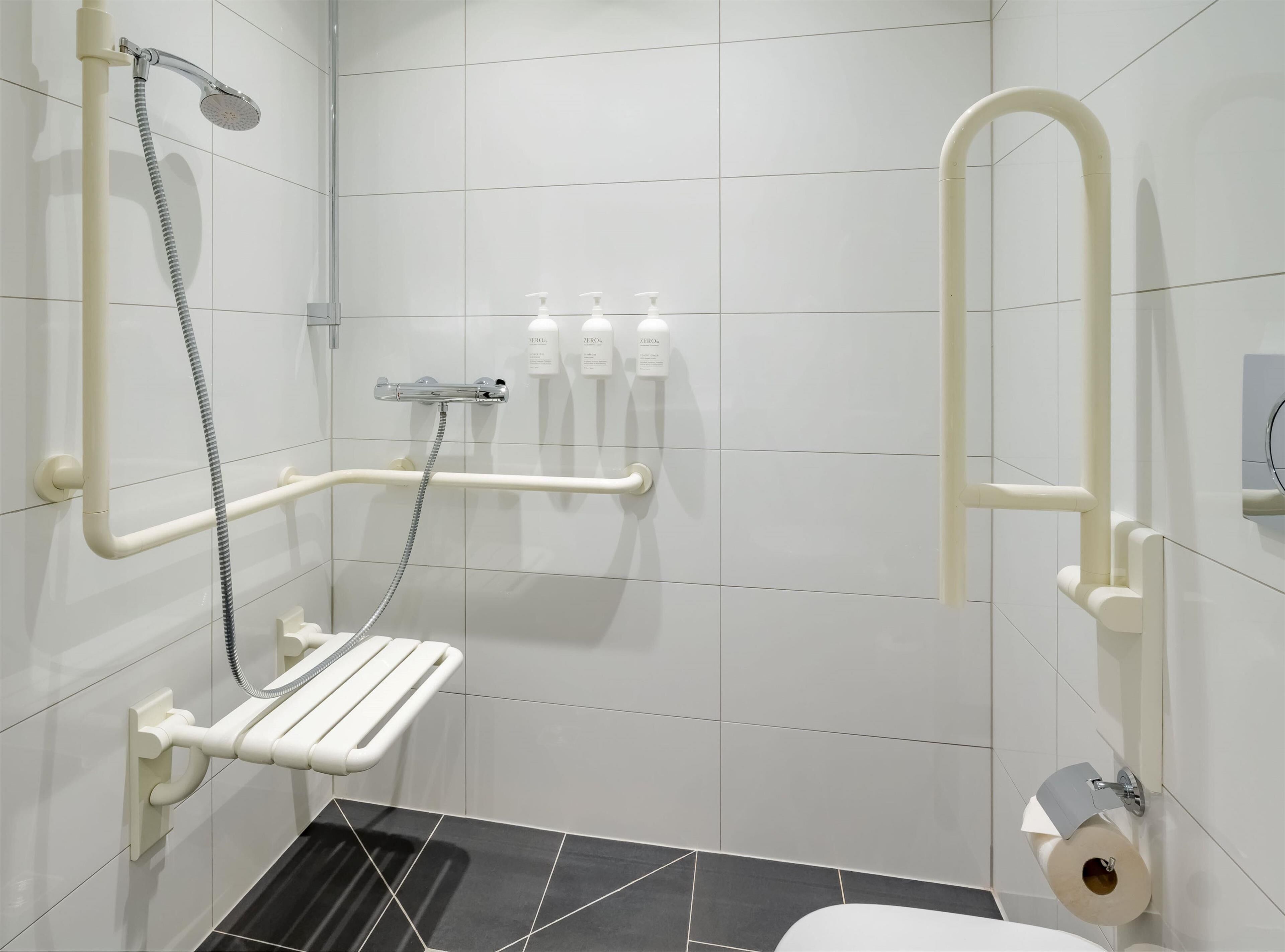 Ein modernes Badezimmer mit Dusche, Haltegriffen, Toilette und einem Handtrockner.
