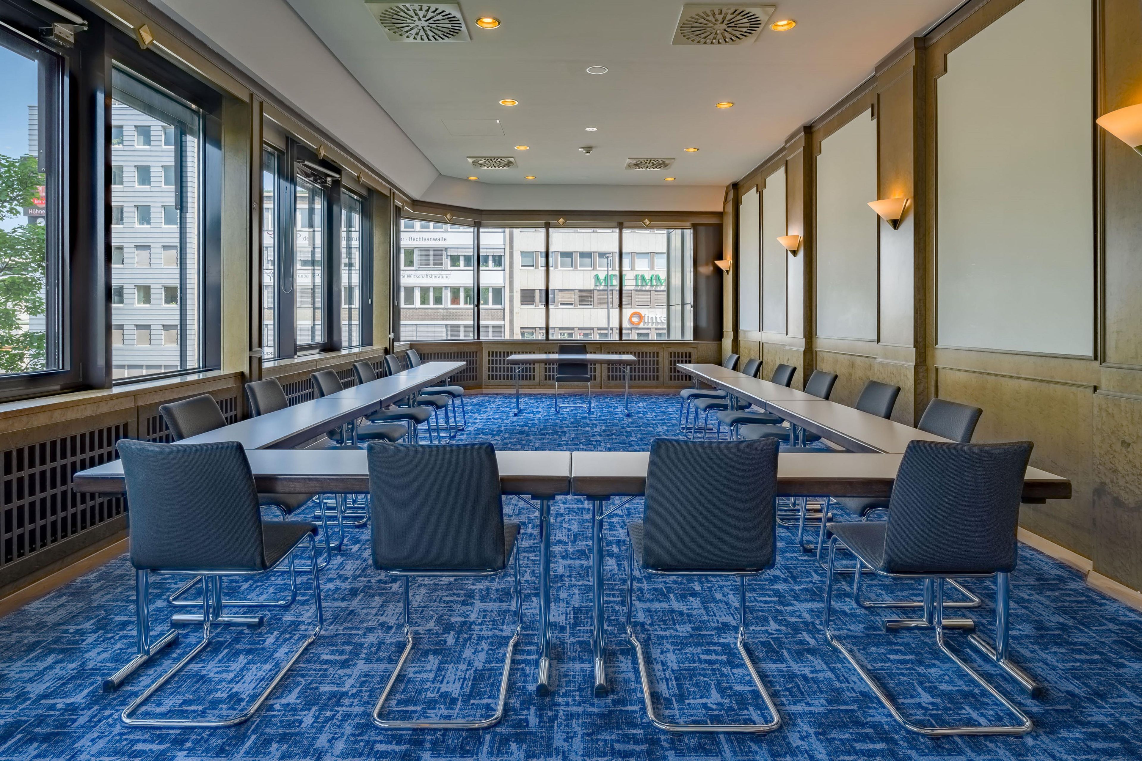 A conference room with a long table and chairs, large windows, and a blue carpet.