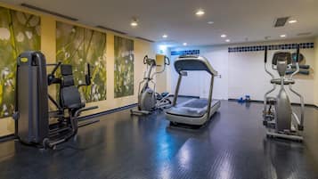 Un gimnasio con cintas de correr, máquinas de pesas y una pared con un mural floral.