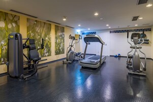 Un gimnasio con cintas de correr, máquinas de pesas y una pared con un mural floral.