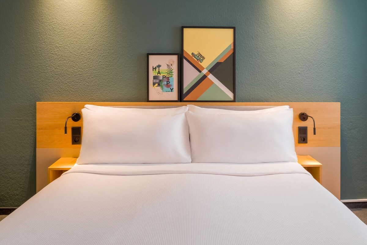 A neatly made bed with white linens, a wooden headboard, and two bedside tables with lamps.