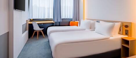 Quarto de hotel com cama, escrivaninha, cadeira e televisão.