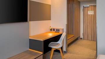 Una habitación de hotel moderna con un escritorio de madera, una silla blanca, un televisor de pantalla plana montado en la pared y un armario de madera.