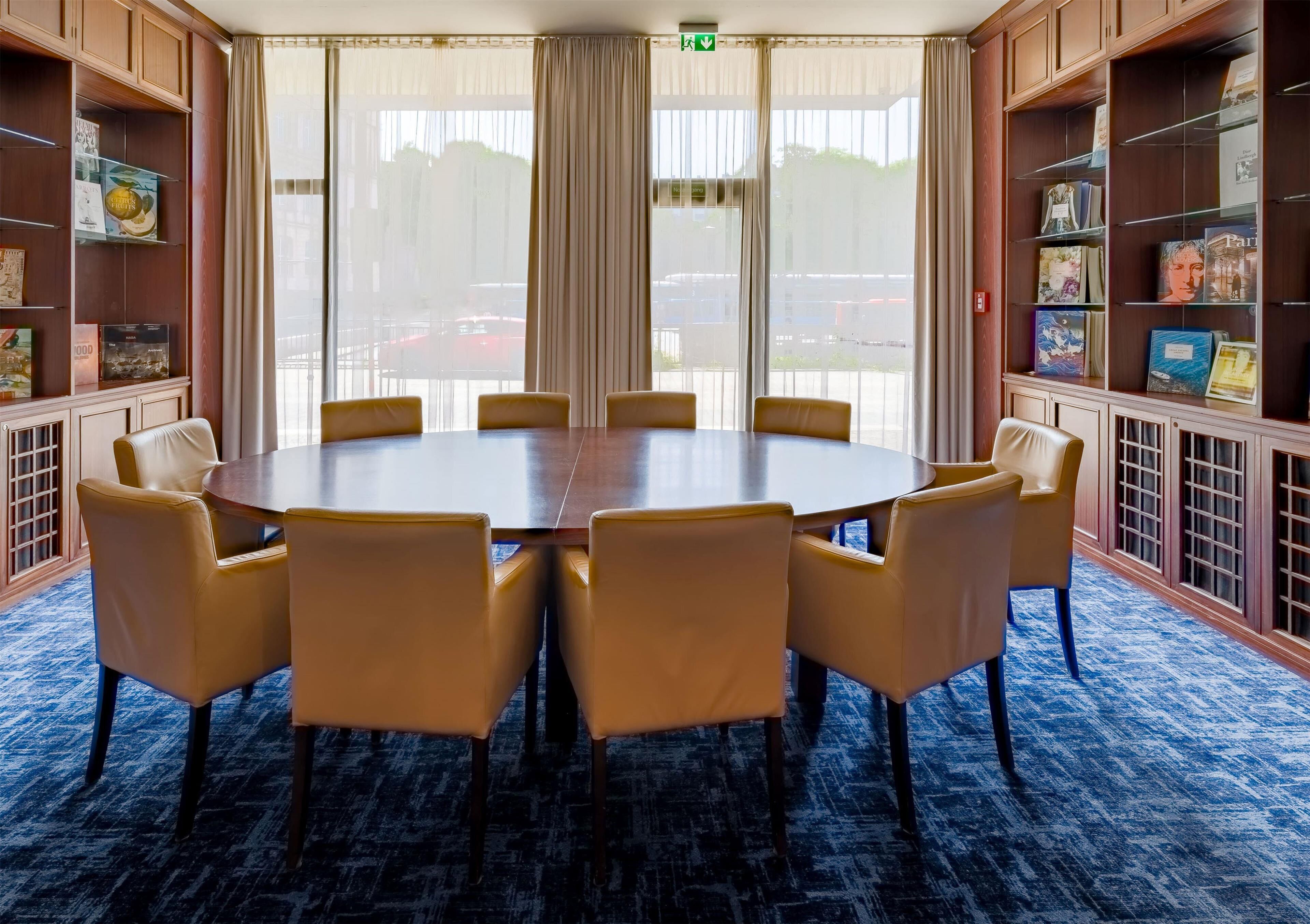 Ein Konferenzraum mit rundem Tisch und sechs Stühlen, umgeben von Bücherregalen.