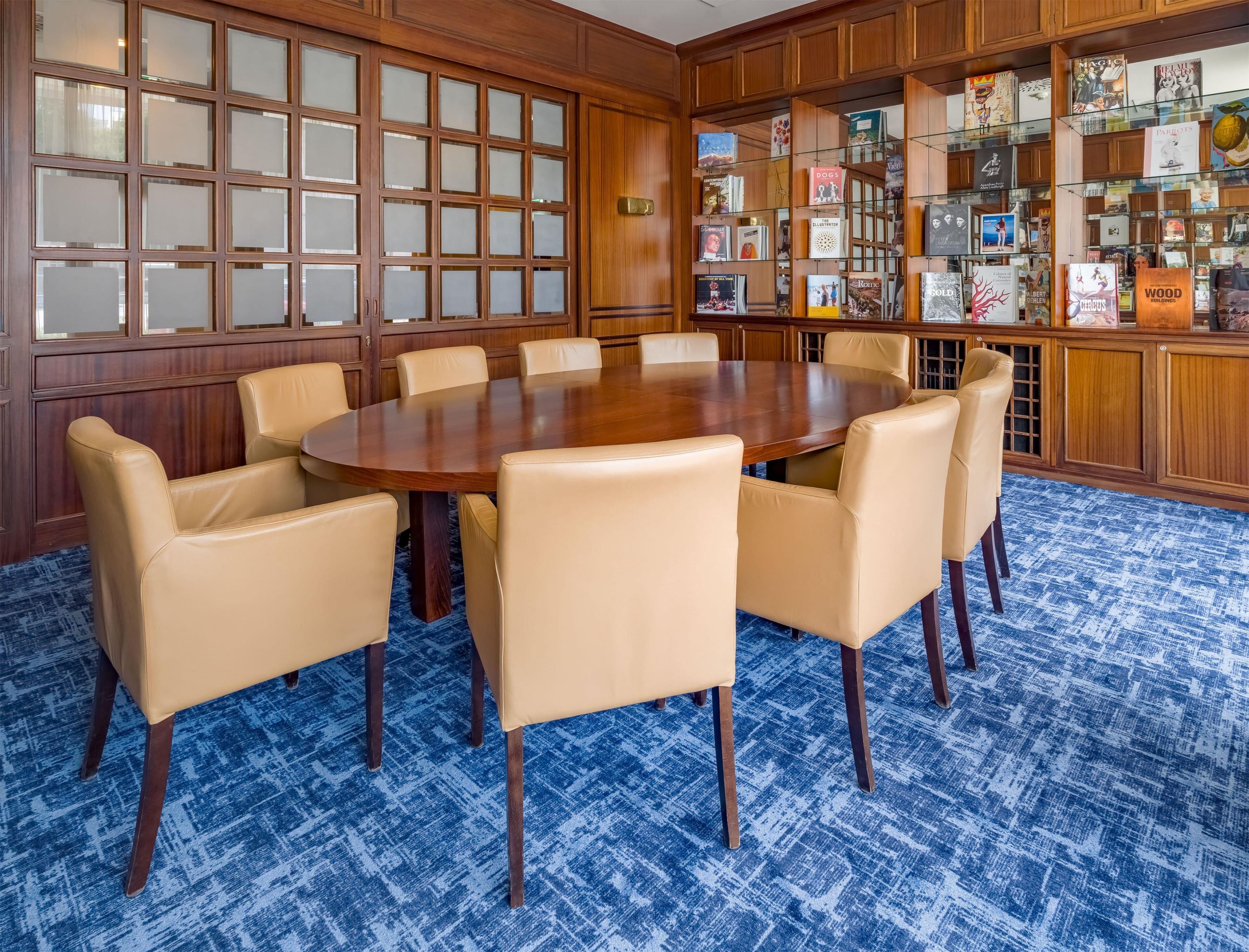 A conference room with a round table, beige chairs, and a blue patterned carpet.