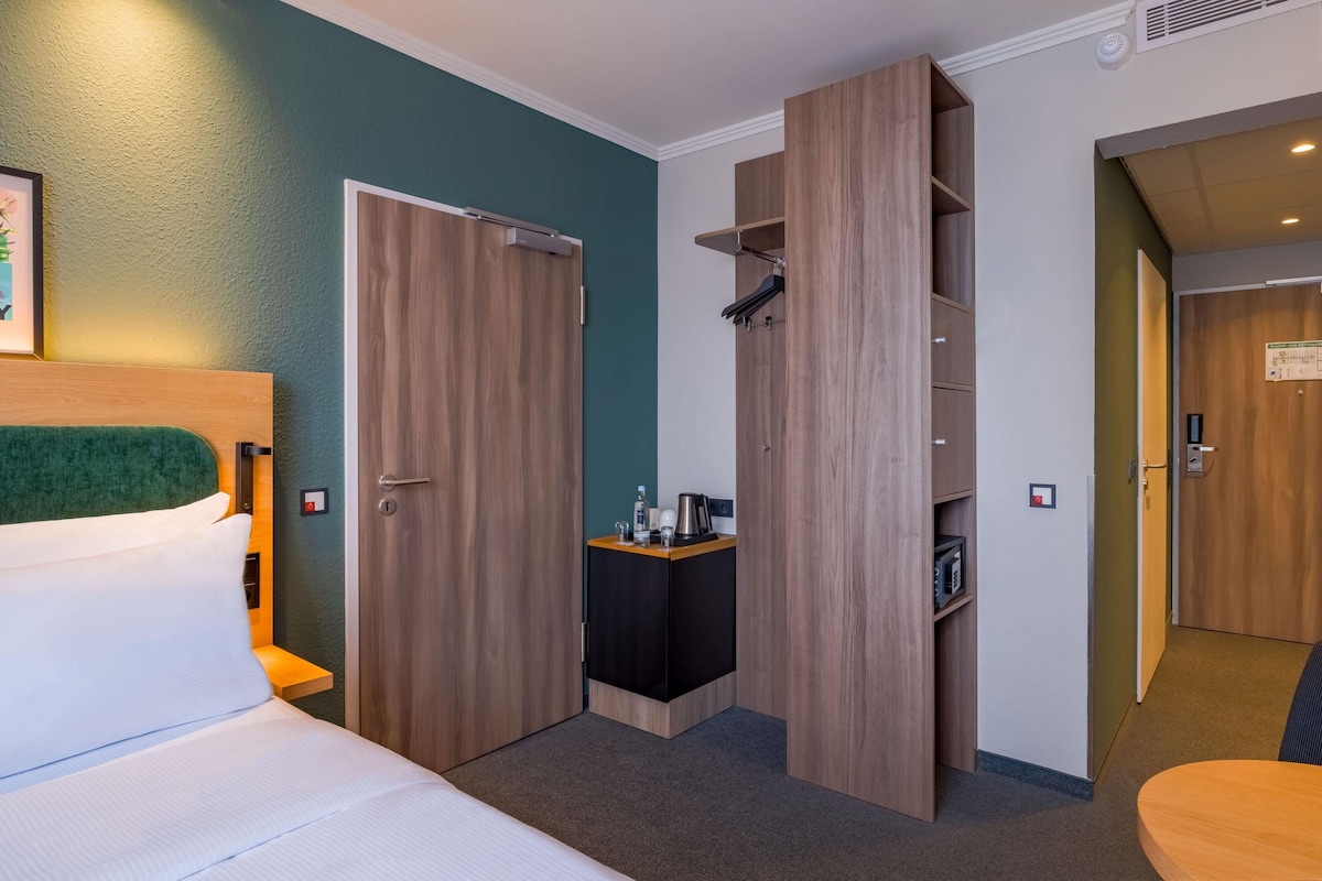 A hotel room with a bed, a desk, a wardrobe, and a door leading to another room.