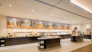 A modern hotel lobby with a buffet area, a large mural, and a reception desk.