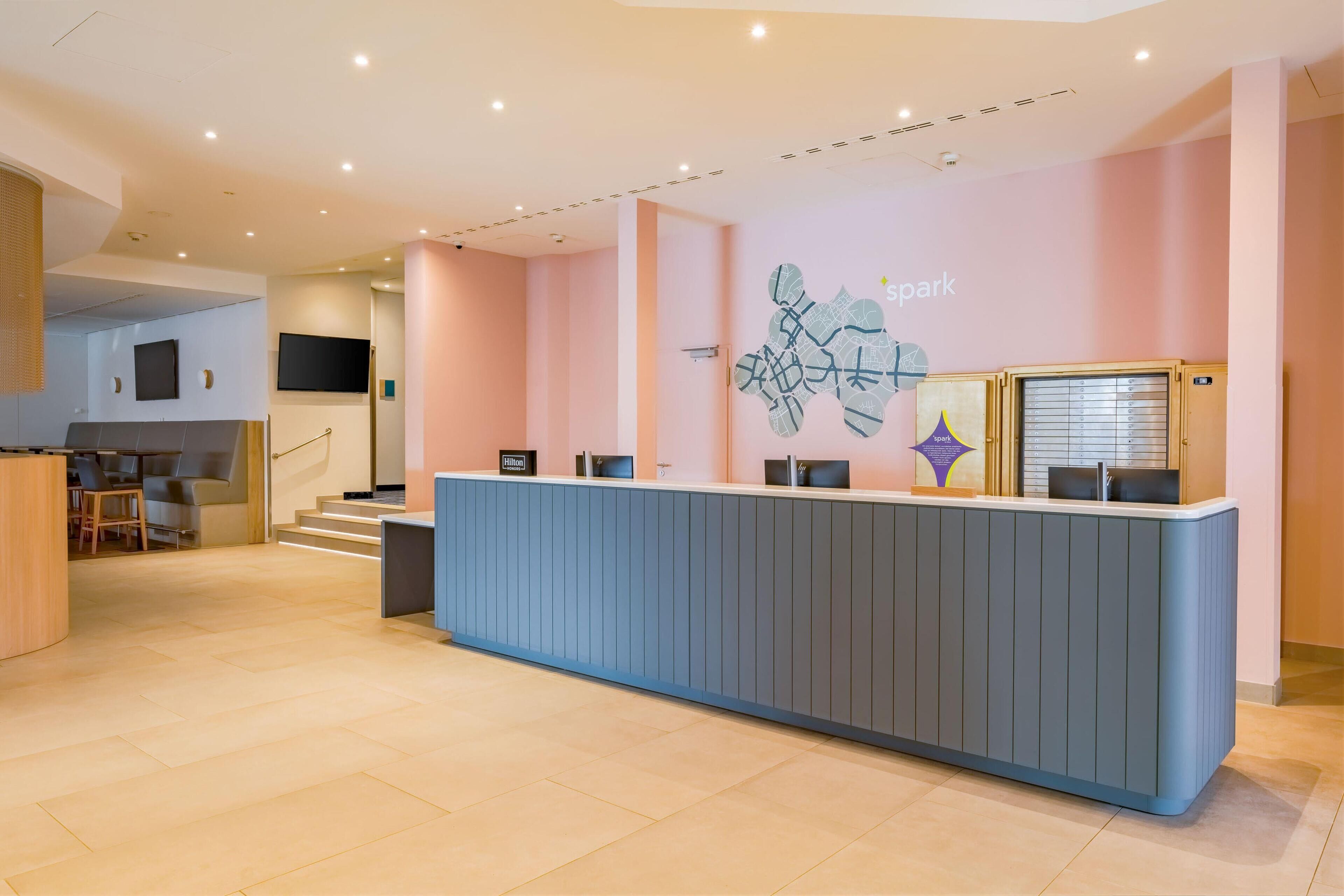 A reception desk with a blue counter, a staircase, and a wall-mounted screen.