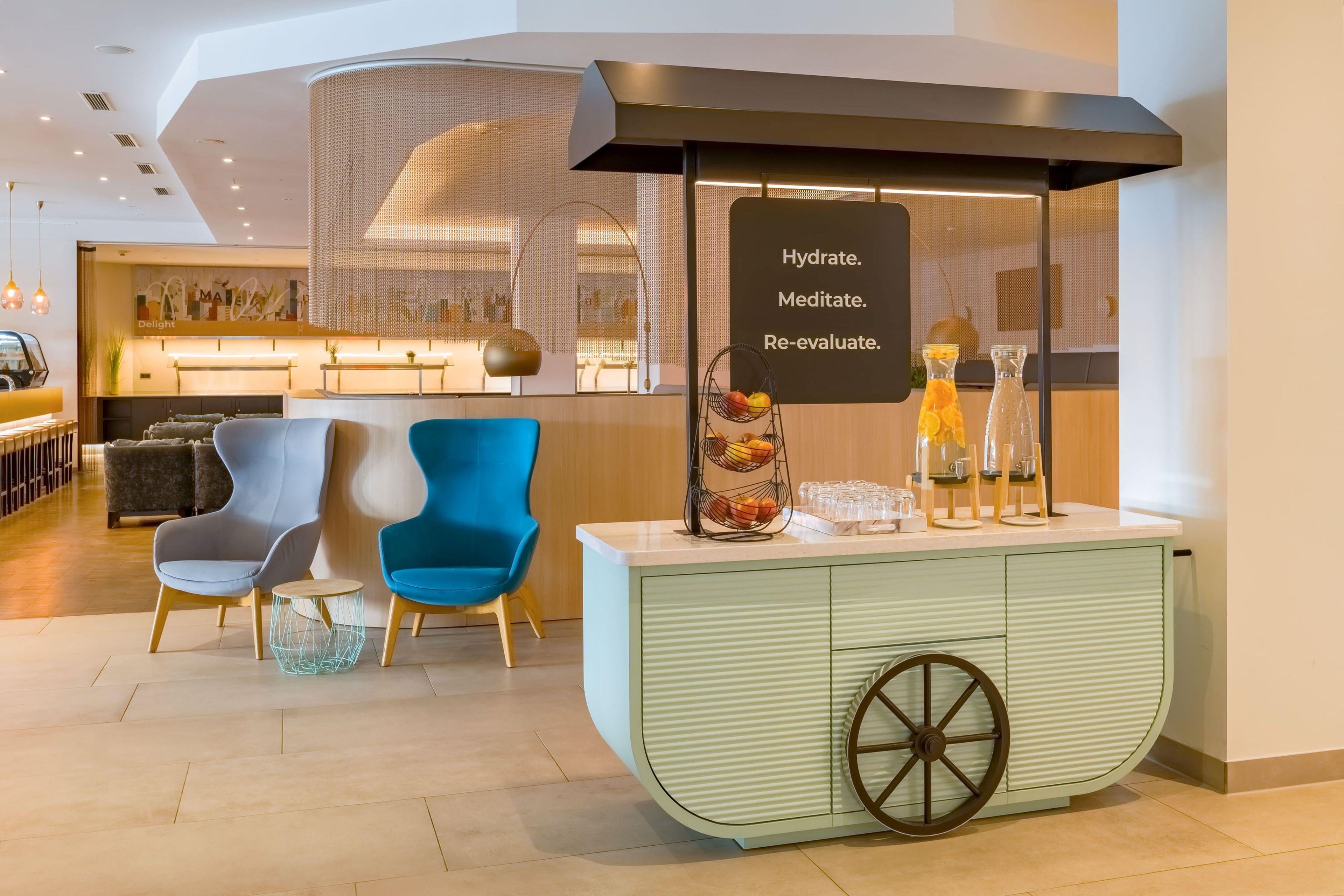 A modern lounge area with seating, a refreshment station, and a sign promoting hydration and meditation.
