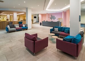 A modern hotel lobby with seating areas, a reception desk, and a staircase leading to upper floors. - Spark by Hilton Wuppertal City Centre (Wuppertal)