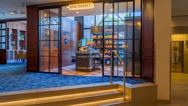 A hotel lobby with a 'Mini Market' sign, a reception desk, and a staircase leading to the upper floors.