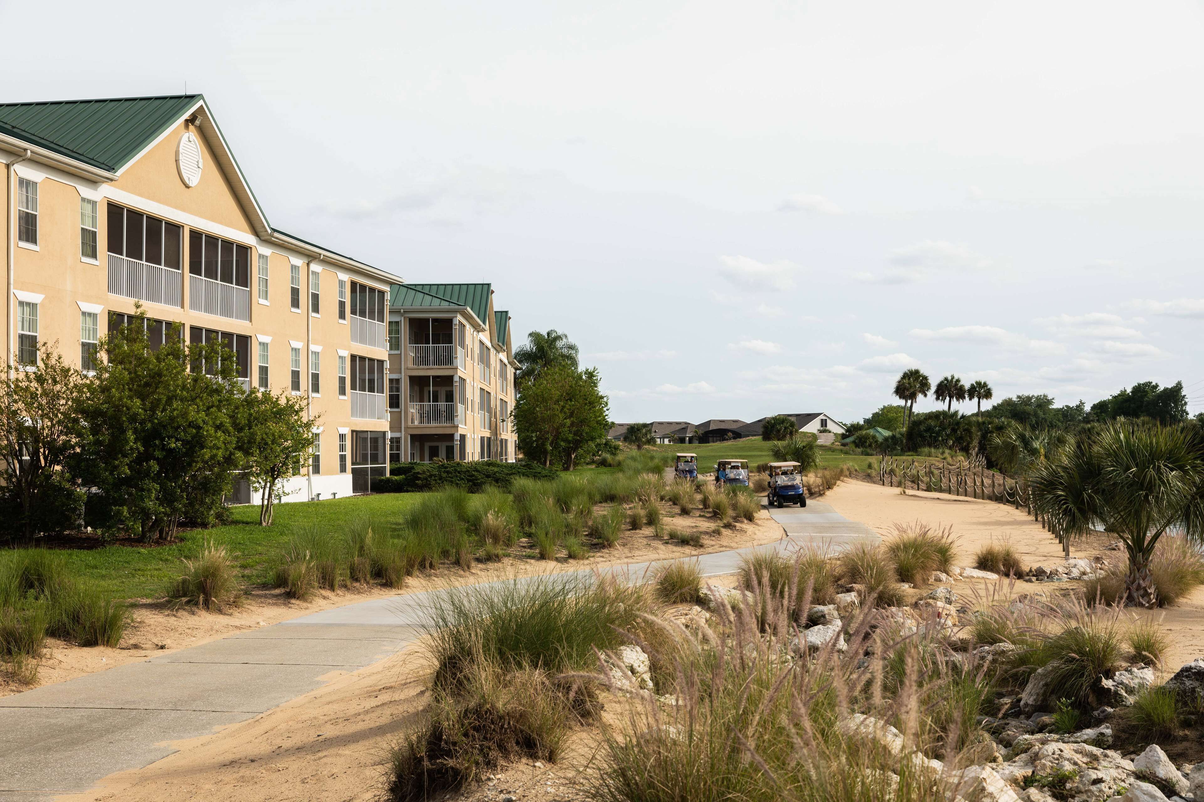 A multi-story hotel with balconies, a paved pathway, and surrounding natural landscape.
