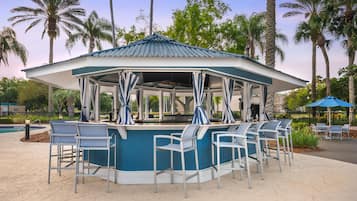 A gazebo with a blue and white color scheme, surrounded by outdoor bar seating and palm trees.