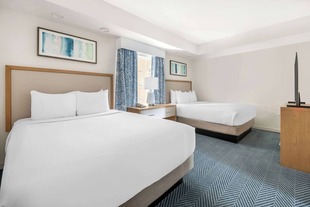 A hotel room with two beds, a nightstand, a desk, and a TV.