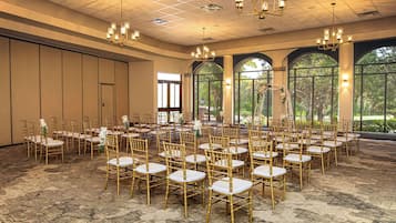 A large hall with rows of gold chairs and tables, large windows, and chandeliers.