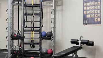 Een sportschool met een optrekstang, kettlebells, medische ballen en een bankdrukapparaat.