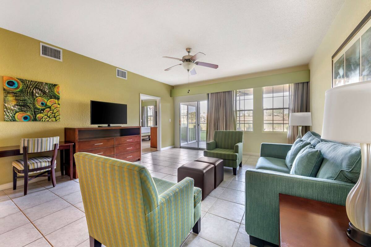 A spacious living room with a television, a ceiling fan, and a large window with curtains.
