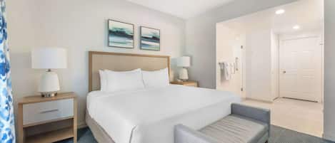 A hotel room with a large bed, two bedside tables with lamps, a chair, and a door leading to another room.