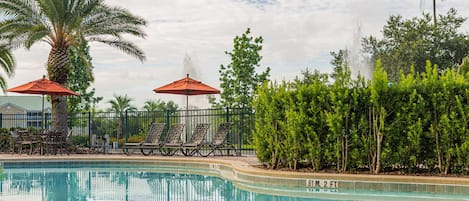 A swimming pool with lounge chairs and umbrellas, surrounded by palm trees and greenery.