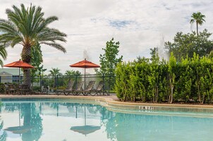 Una piscina con lettini e ombrelloni, circondata da palme e vegetazione.