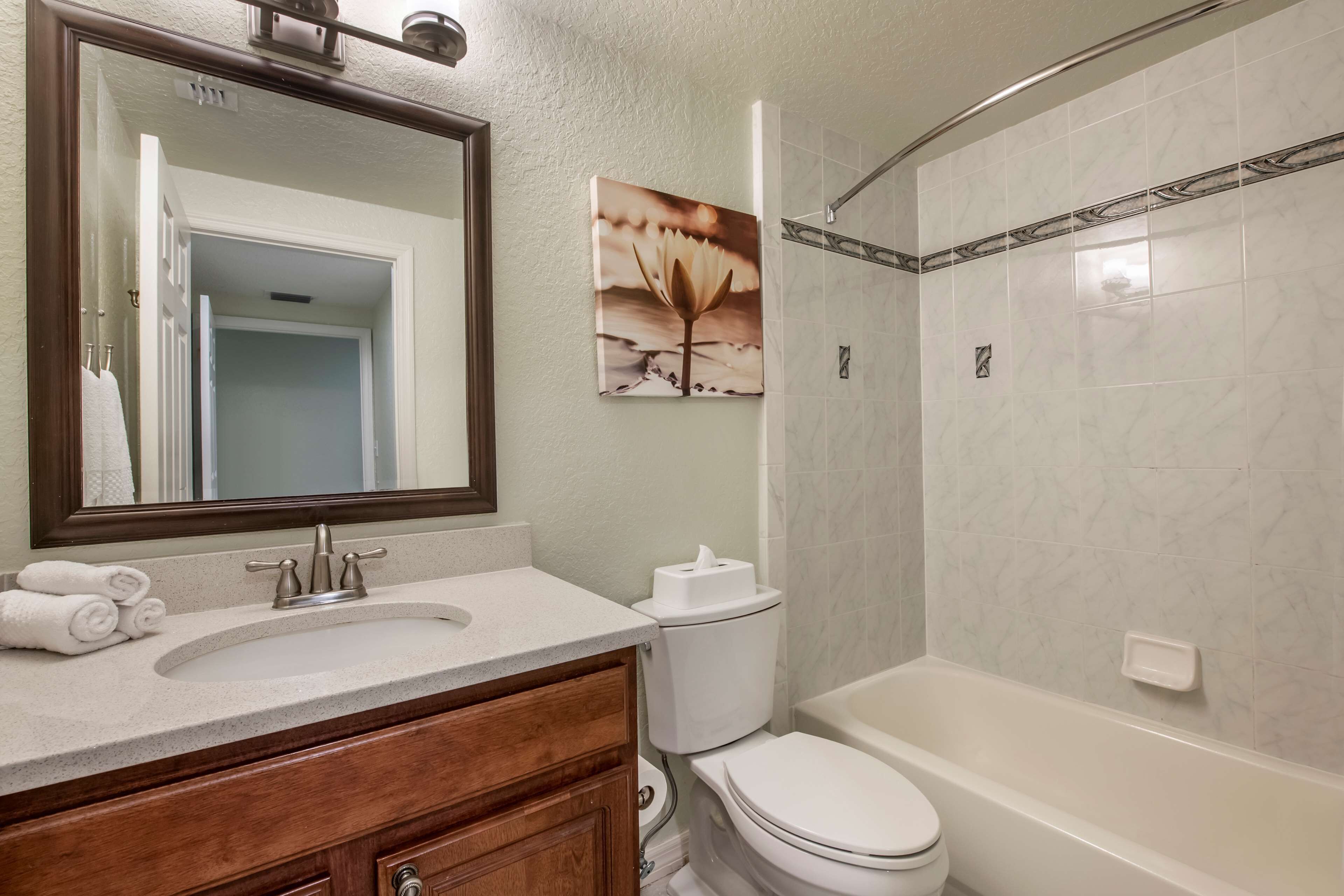 Un baño con lavabo, inodoro y bañera. Hay un espejo sobre el lavabo y un cuadro en la pared.