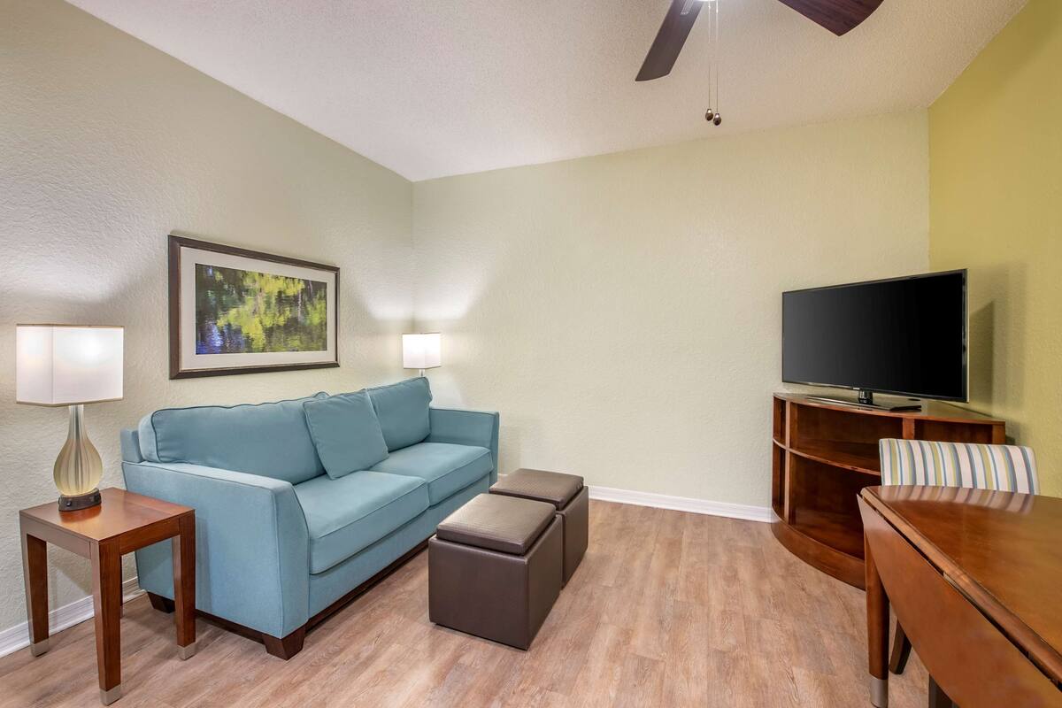 A living room with a blue sofa, a wooden coffee table, a TV on a stand, and a lamp on a side table.