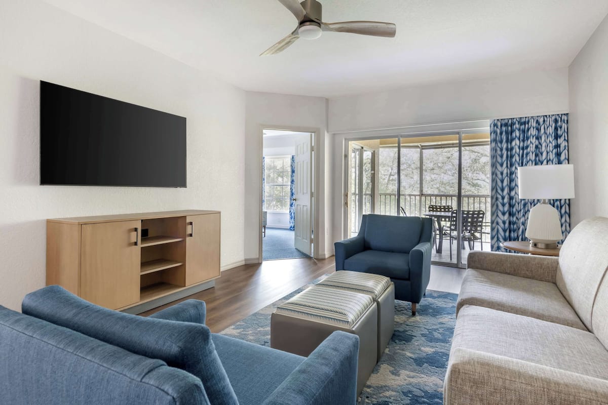 A modern living room with a flat-screen TV, a wooden cabinet, a blue armchair, a beige sofa, and a patterned rug.