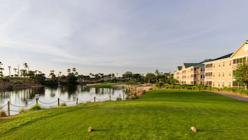 Un parcours de golf avec un étang, une clôture et un bâtiment à plusieurs étages doté de balcons.