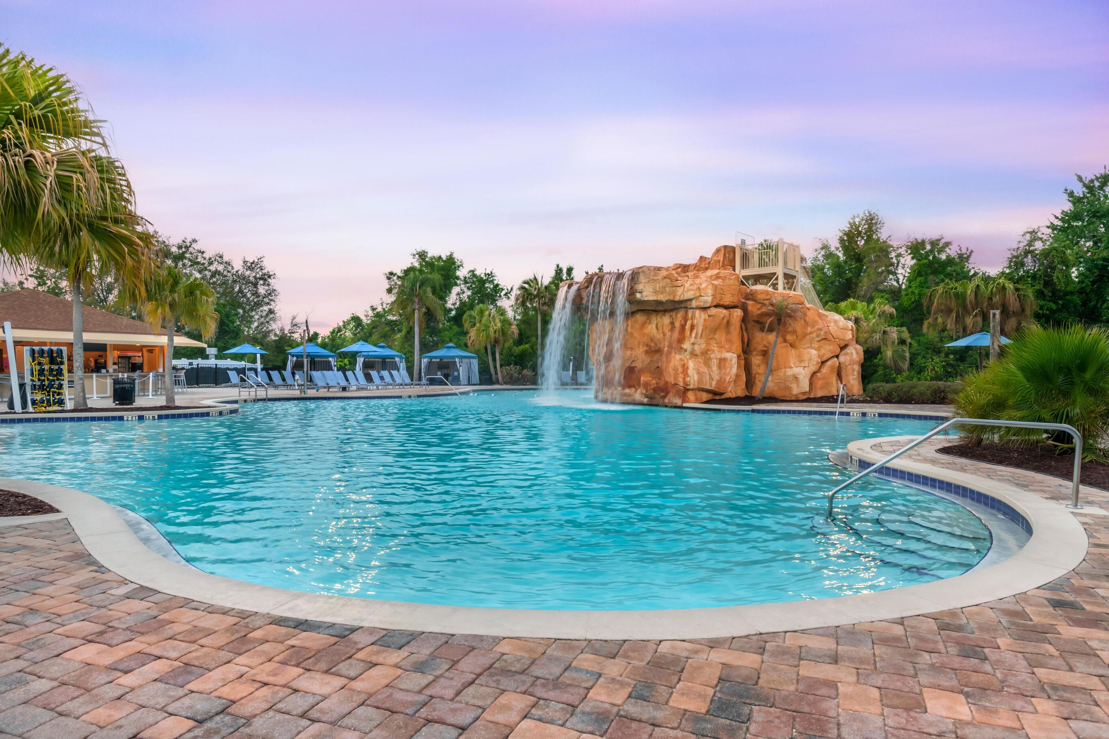A swimming pool with a waterfall feature, lounge chairs, and a building with a covered area.