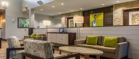 A modern lobby with a high ceiling, recessed lighting, a stone accent wall, and a seating area with patterned chairs and a sofa with green cushions.