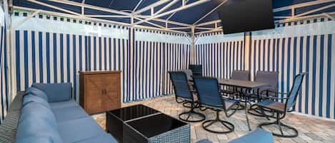 An outdoor patio with a sofa, chairs, a table, and a TV screen.