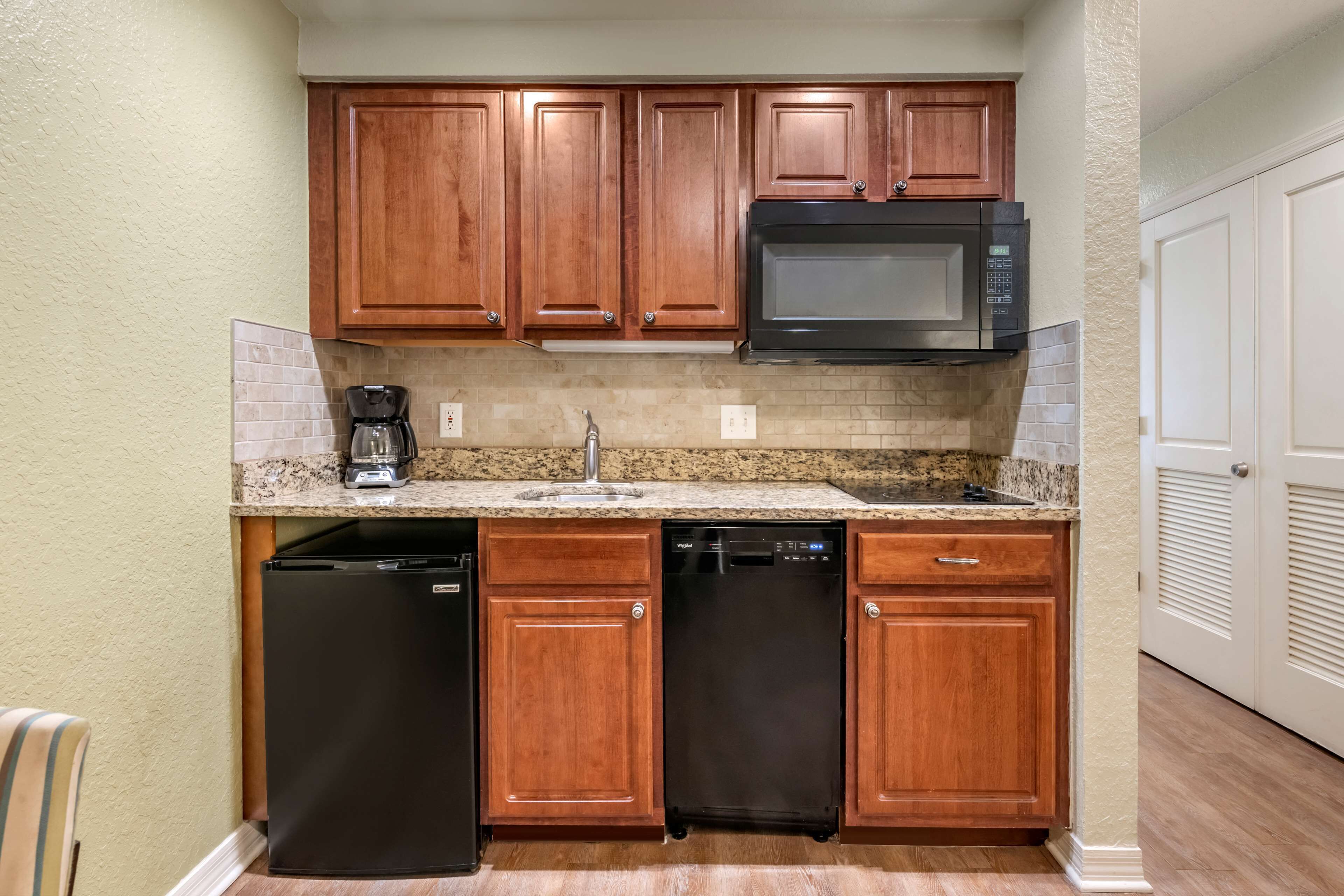 A compact kitchen with wooden cabinets, a built-in microwave, a coffee maker, and a dishwasher.