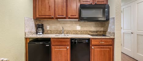 A compact kitchen with wooden cabinets, a built-in microwave, a coffee maker, and a dishwasher.