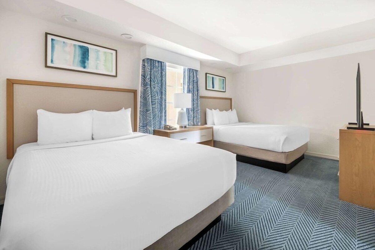 A hotel room with two beds, a nightstand, a desk, and a television.