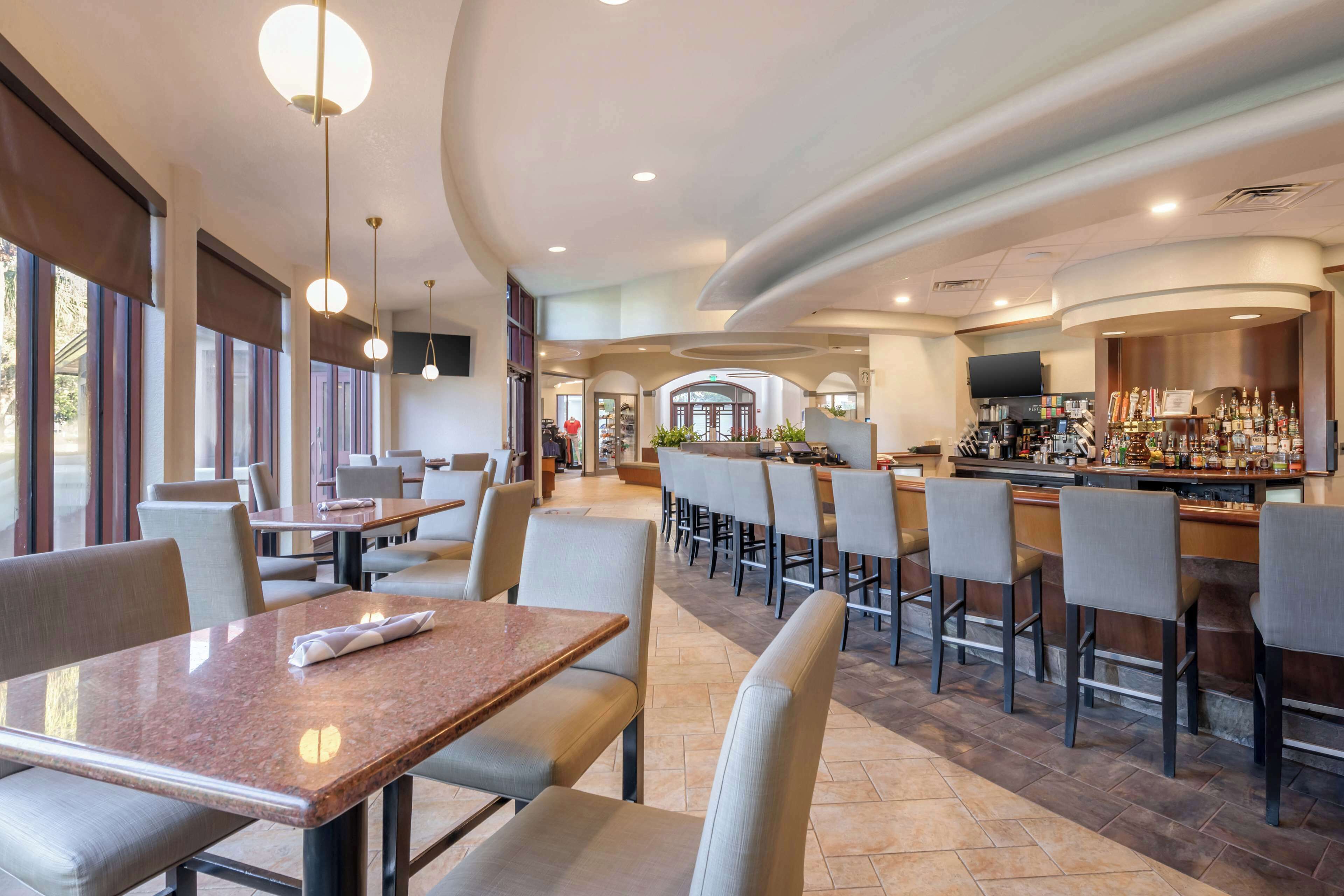 A modern restaurant with a bar area, featuring high tables, bar stools, and a television mounted above the bar.