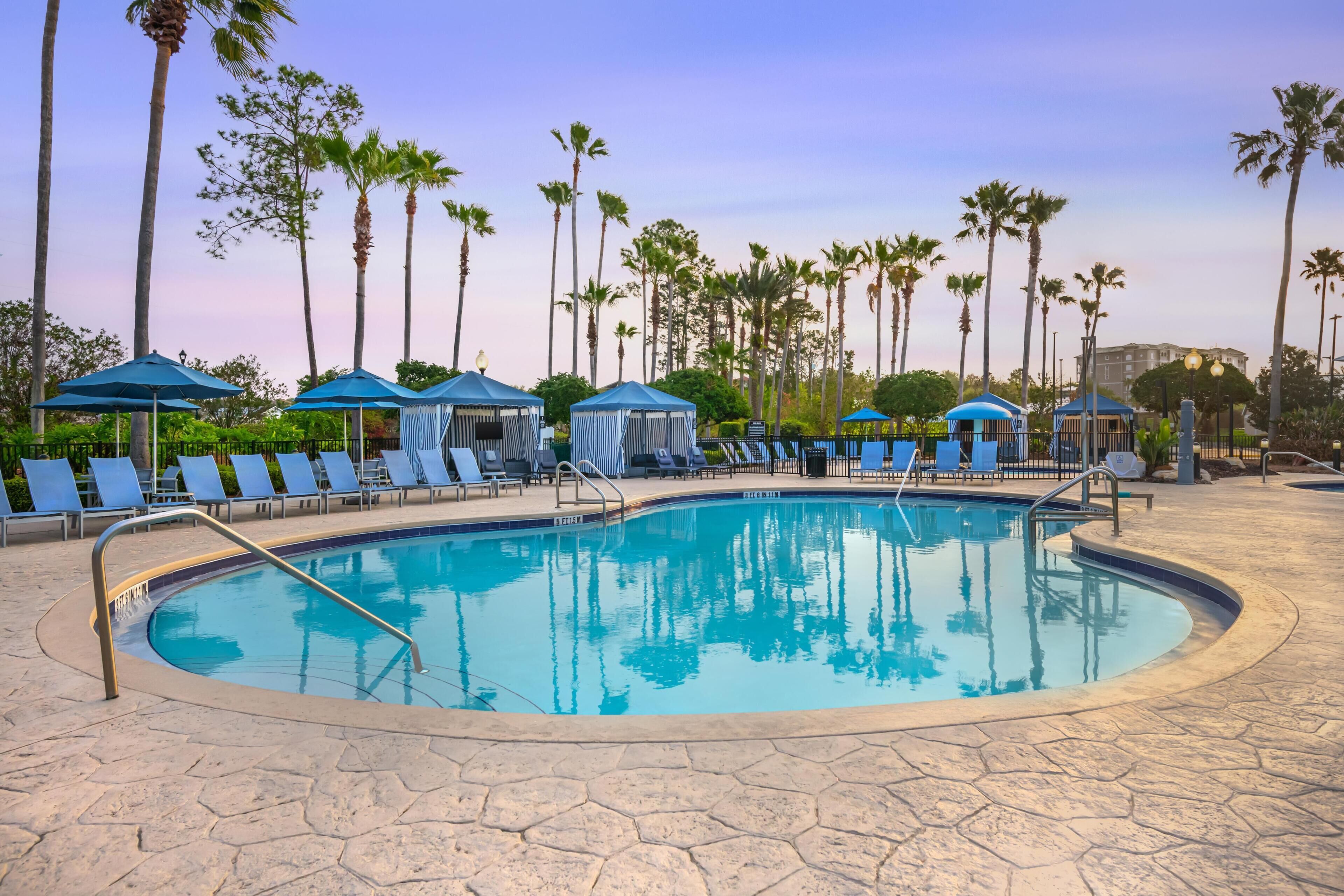 A swimming pool with lounge chairs and umbrellas, surrounded by palm trees.