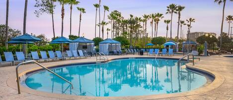 A swimming pool with lounge chairs and umbrellas, surrounded by palm trees.