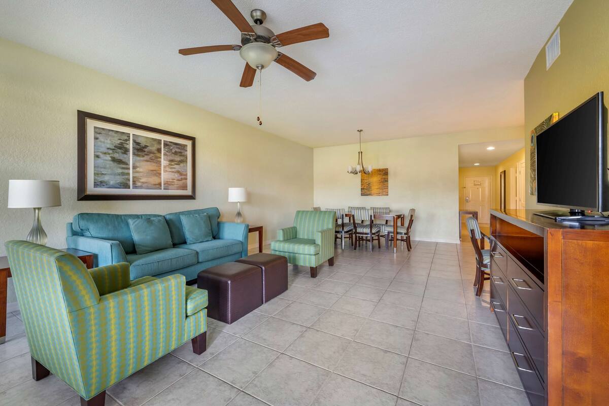 A living room with a sofa, armchairs, a coffee table, a TV, and a dining area with chairs and a table.