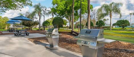 Des barbecues d’extérieur, des tables de pique-nique et un parasol bleu, le tout installé dans un parc.