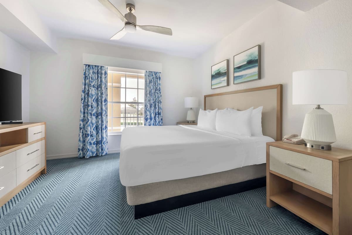 A hotel room with a bed, a desk, a TV, a lamp, and a window with curtains.