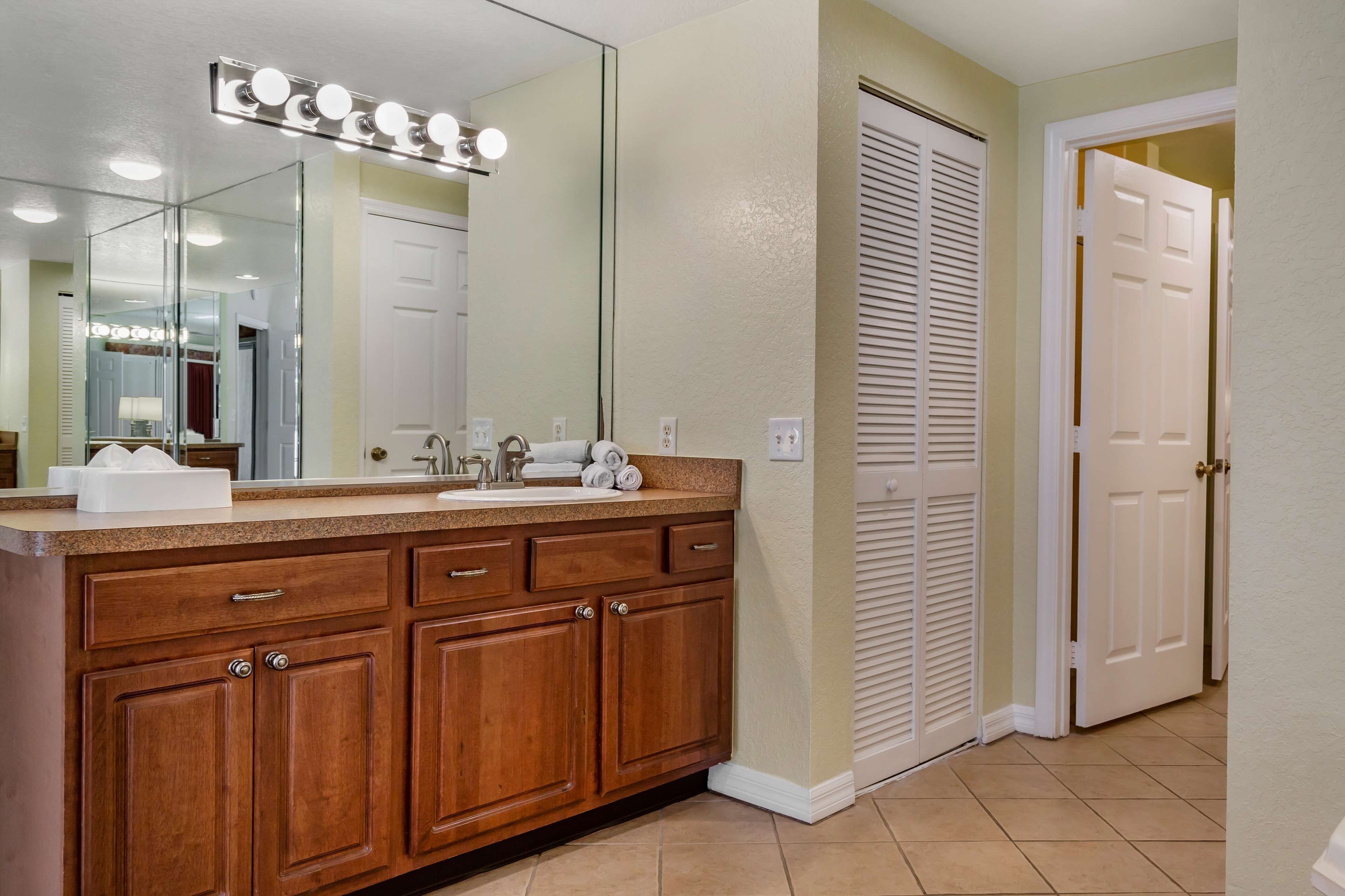 A bathroom with a wooden vanity, a large mirror with lights, a sink, and a towel rack.