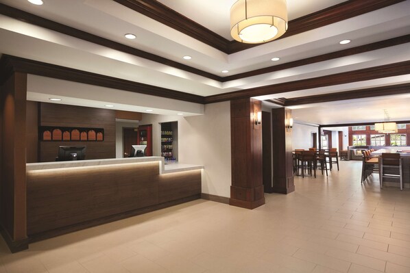 A reception area with a wooden reception desk, a counter, and a seating area with tables and chairs. - HYATT house Pleasant Hill (Pleasant Hill)
