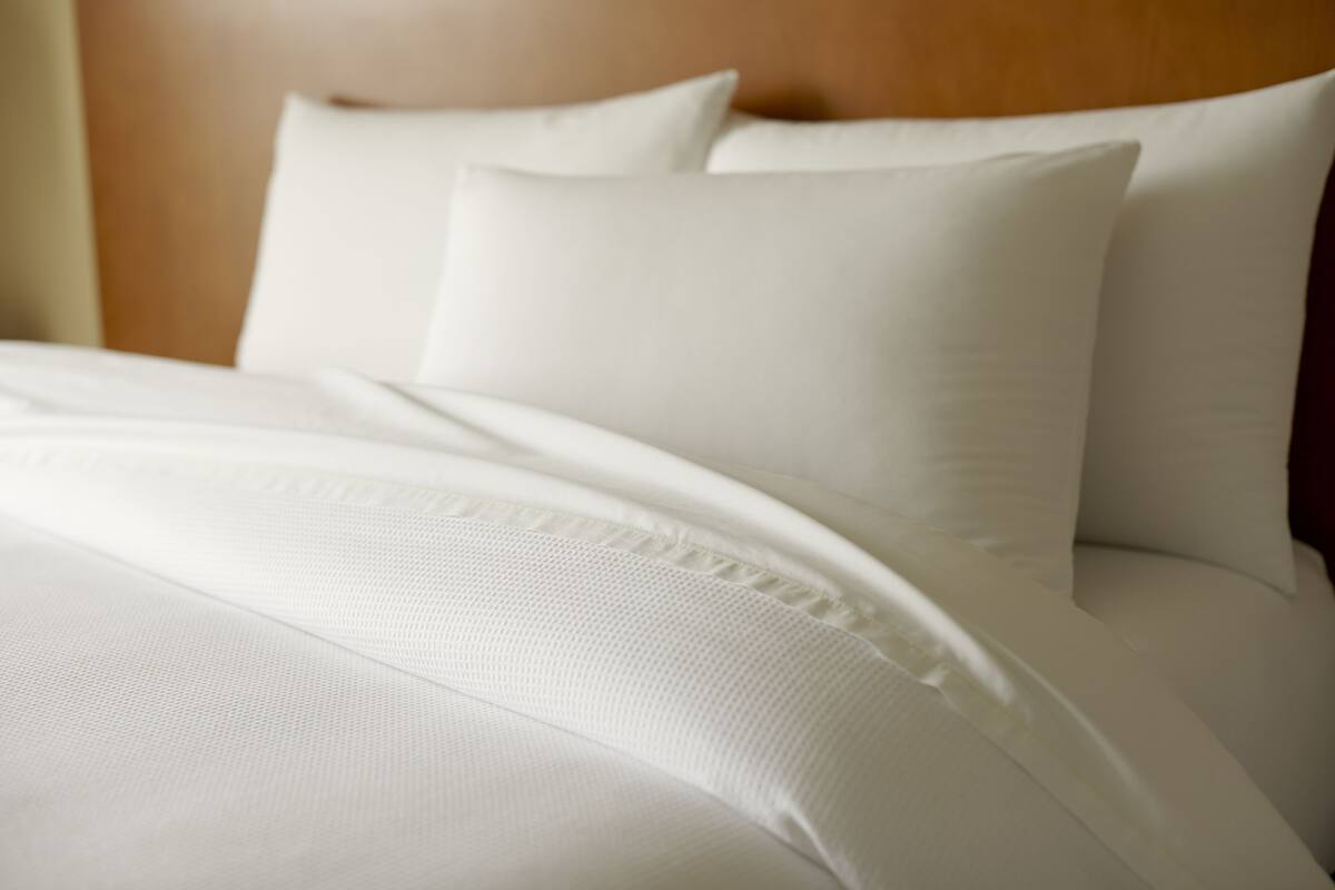 A neatly made bed with white linens and pillows.
