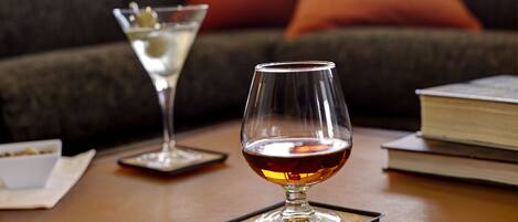 A glass of amber liquid on a coaster, a martini glass with a garnish, and a book on a table.
