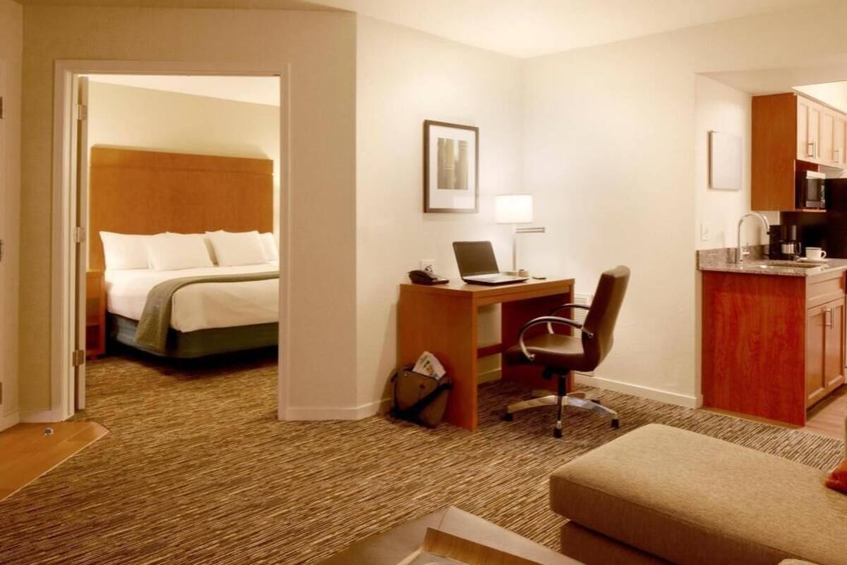 A hotel room with a bed, a desk with a laptop, a chair, a couch, and a kitchenette.