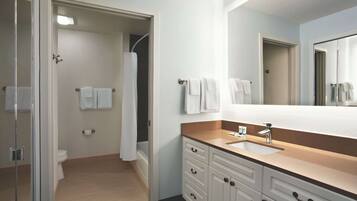 Une salle de bain moderne avec une douche à l’italienne en verre, des toilettes blanches, un lavabo avec un miroir et un meuble-lavabo avec des tiroirs.
