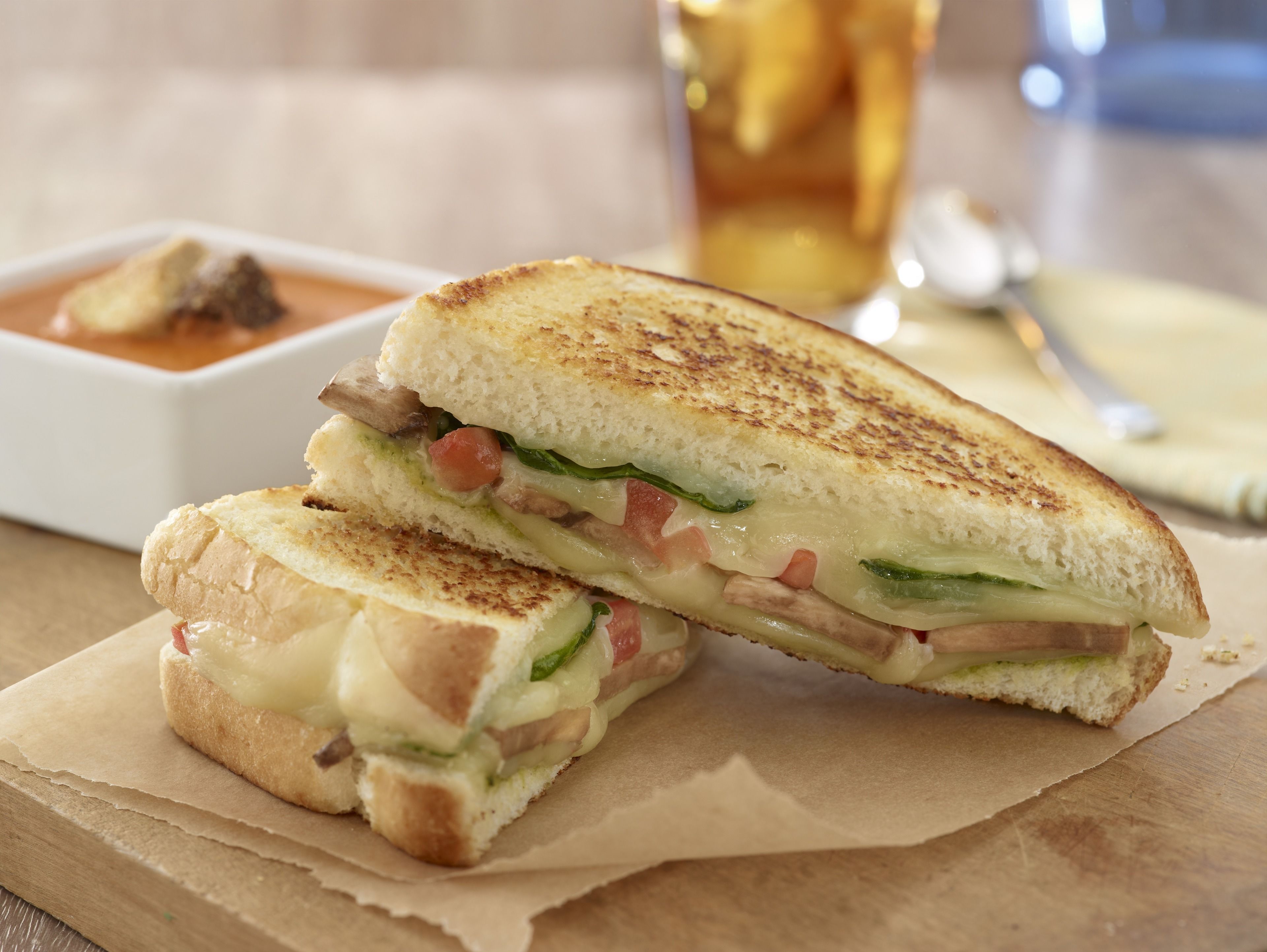 A grilled sandwich with visible ingredients like cheese, vegetables, and meat, placed on a wooden surface with a napkin underneath.