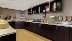 Una cocina moderna con armarios de madera oscura, encimera blanca y diversos alimentos y electrodomésticos.