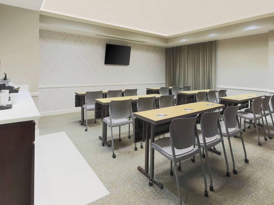 Una sala de conferencias con una larga mesa, sillas, un televisor y un mostrador con una máquina de café.