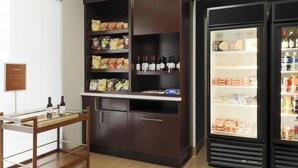Una kitchenette con una mesa de madera, estantes llenos de bocadillos, un enfriador de vino y un refrigerador.